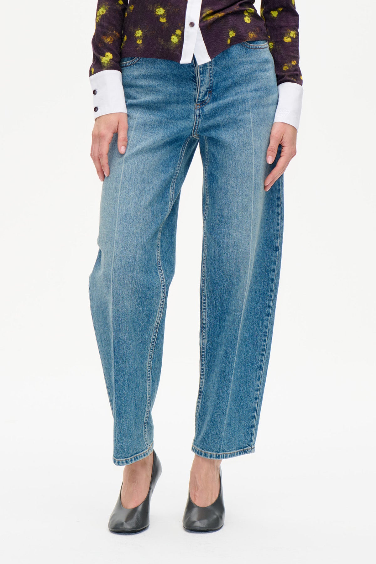 Front detail of blue straight-leg jeans with a faded wash, styled with a dark floral top and black heels.