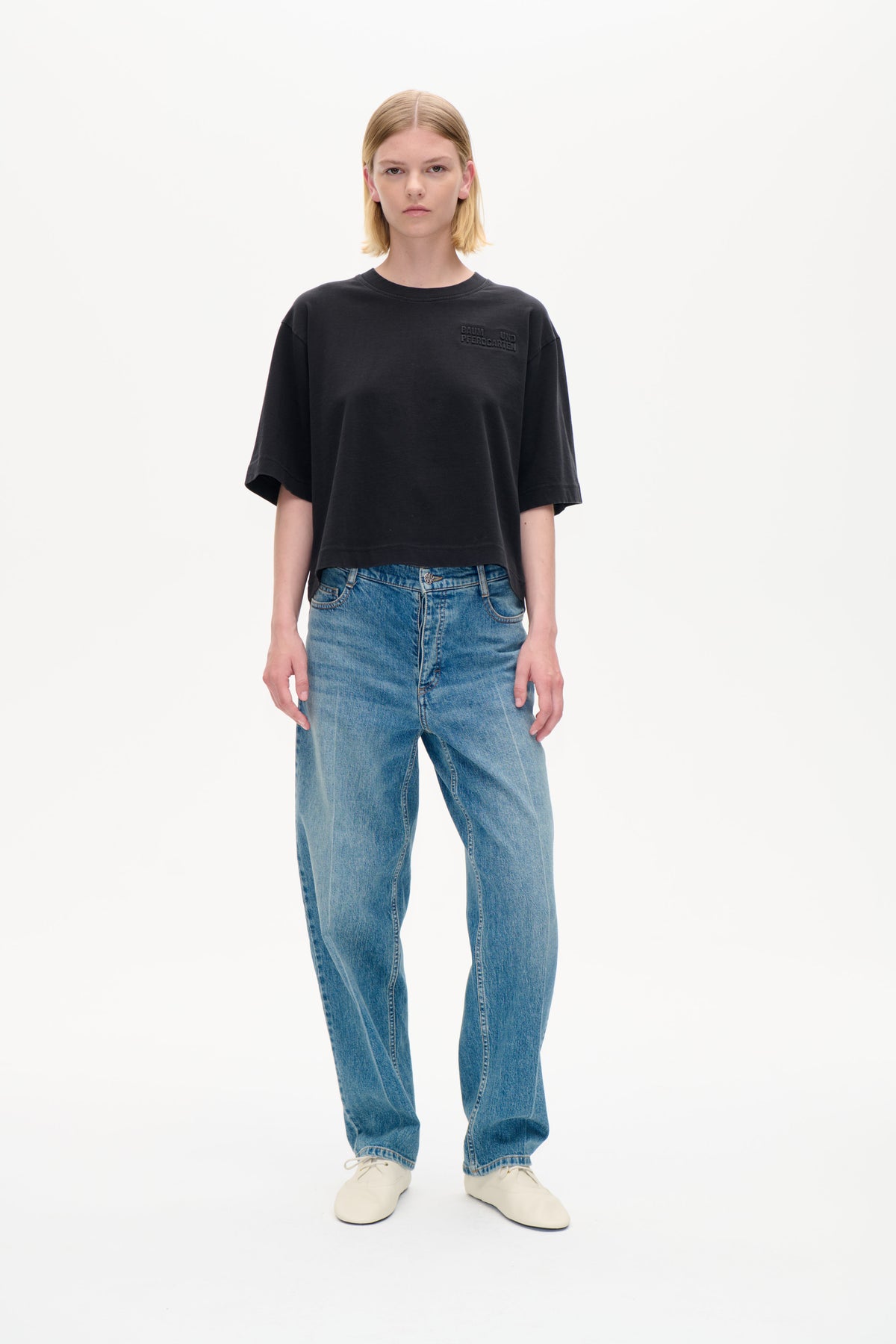 Forfra: en model iført en oversized koksgrå t-shirt med ton-i-ton Baum und Pferdgarten skrift på brystet og blå jeans.