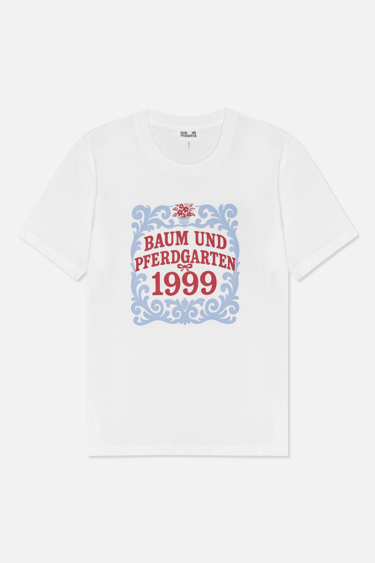 Forfra: en hvid kortærmet t-shirt med en blå ornamentramme, en rød blomsterdetalje og teksten 'Baum und Pferdgarten 1999'.