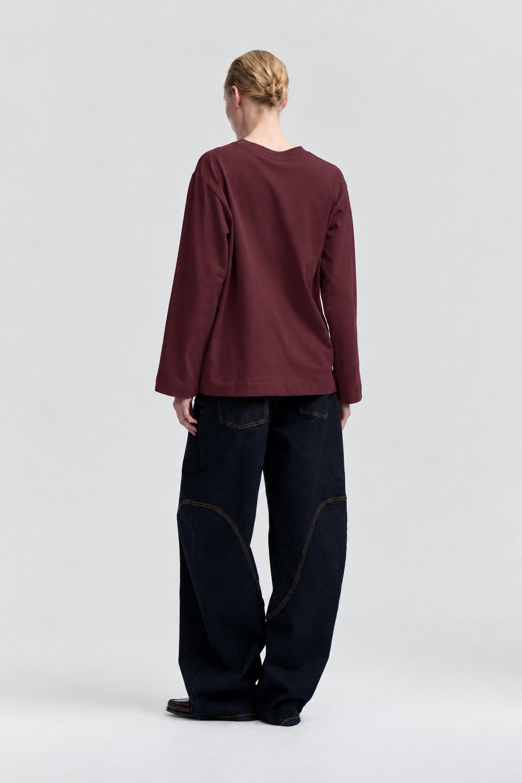Set bagfra af en model iført en ensfarvet, bordeauxfarvet langærmet top med rund hals og mørke wide-leg-jeans.