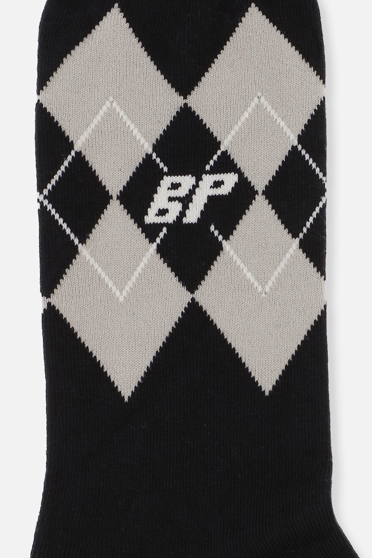 Nærbillede af en sort strikket strømpe med cremefarvede romber i argyle-mønster og en lille monogramdetalje.