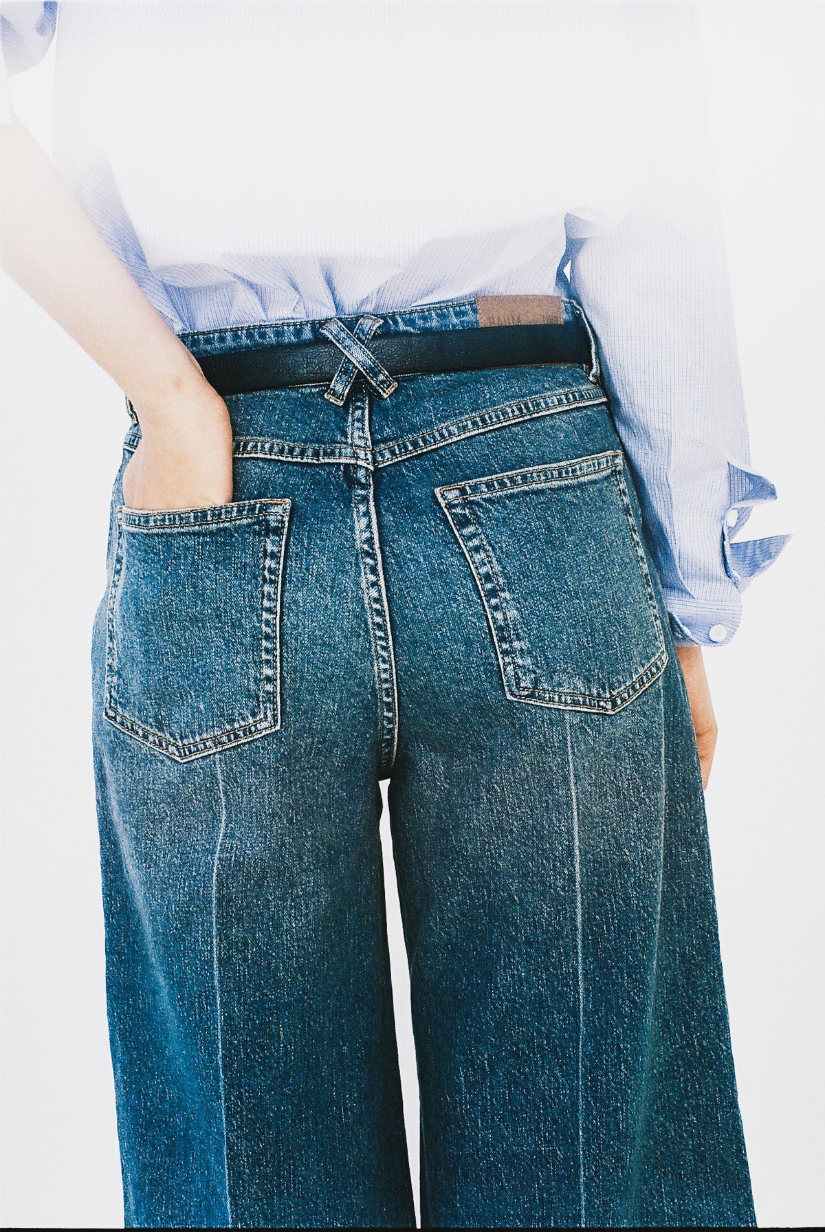 Nærbillede bagfra af blå wide-leg jeans med to påsatte lommer og en lyseblå stribet skjorte stukket ind i linningen