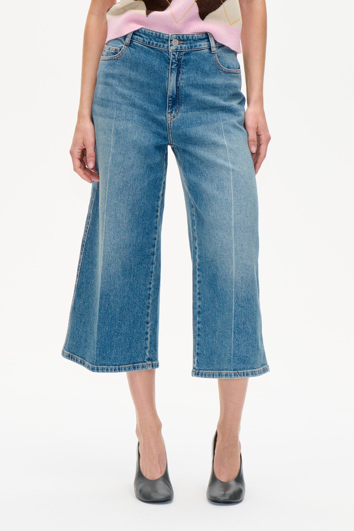 Forfra af cropped blå jeans med vide ben og en fadet vask, stylet med en lyserød og cremefarvet mønstret striktop.