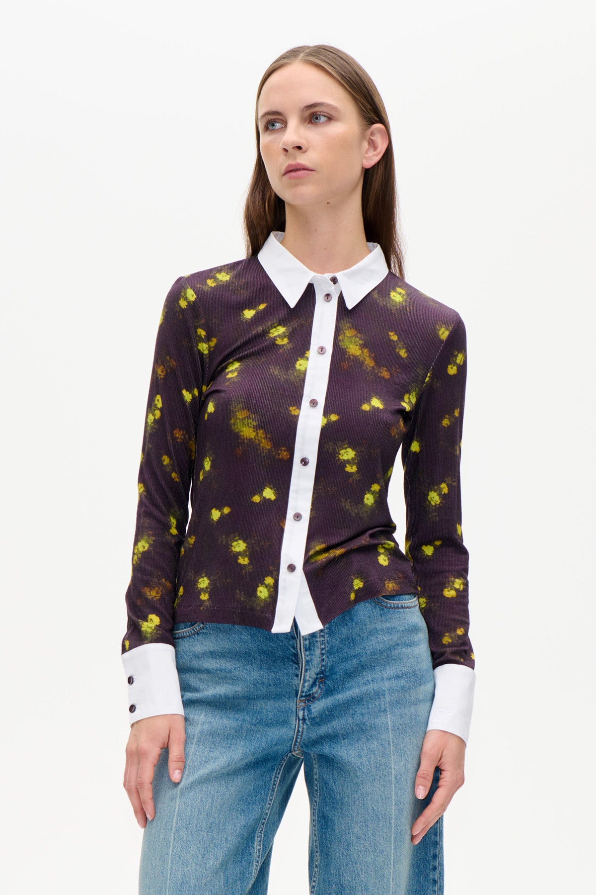Forfra af en mørk plommefarvet cardigan med blomsterprint i lyse gulgrønne toner, hvid krave og manchetter, stylet med blå jeans.