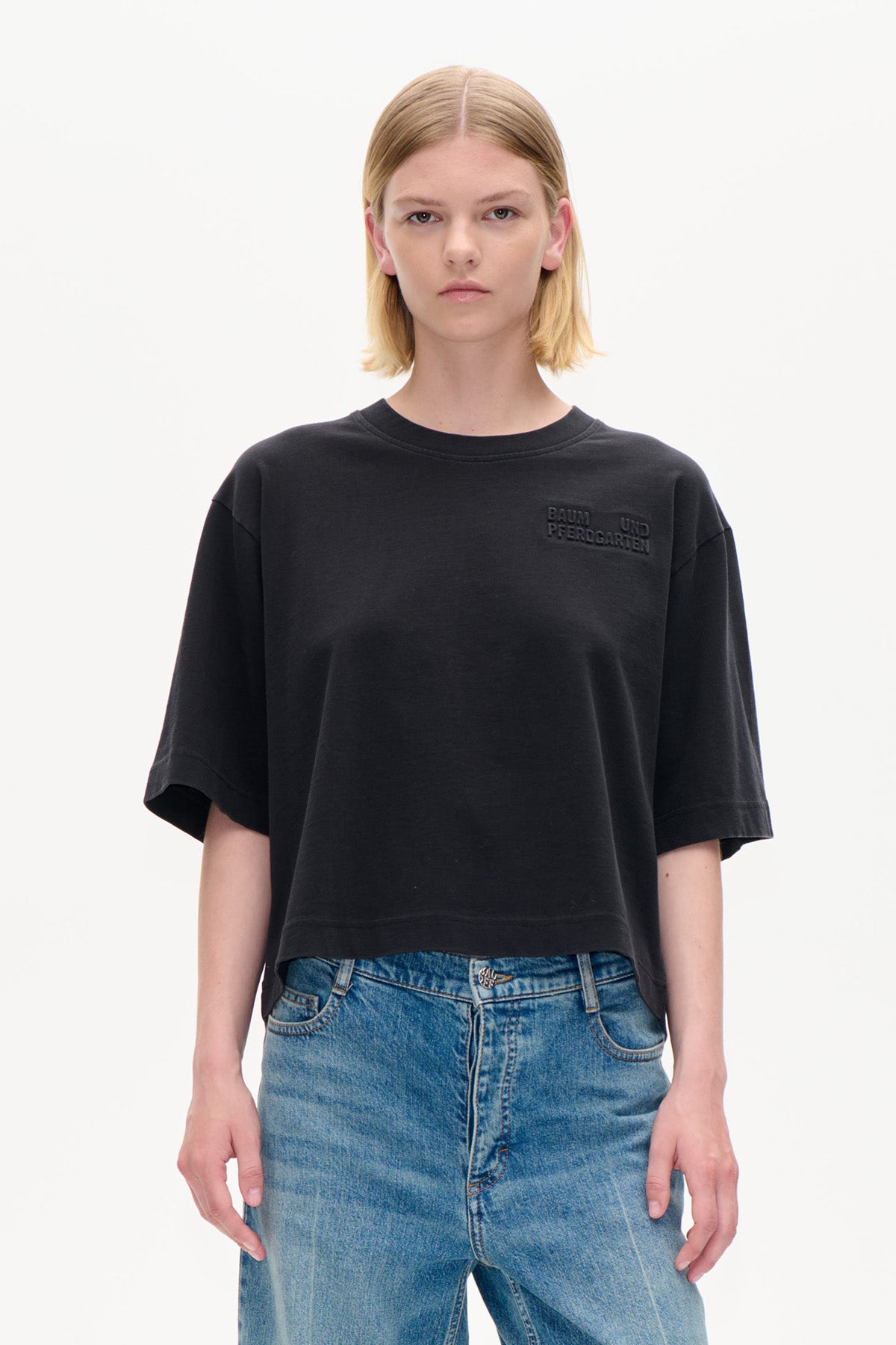 Forfra: sort cropped oversized kortærmet t-shirt med diskret forhøjet tekst på brystet, stylet med blå jeans.