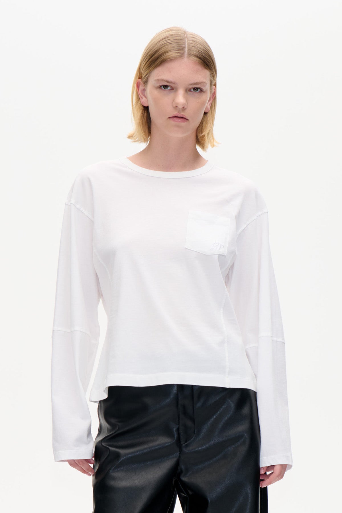 Front view of a white long-sleeved crew-neck top with a chest pocket, styled with black trousers.