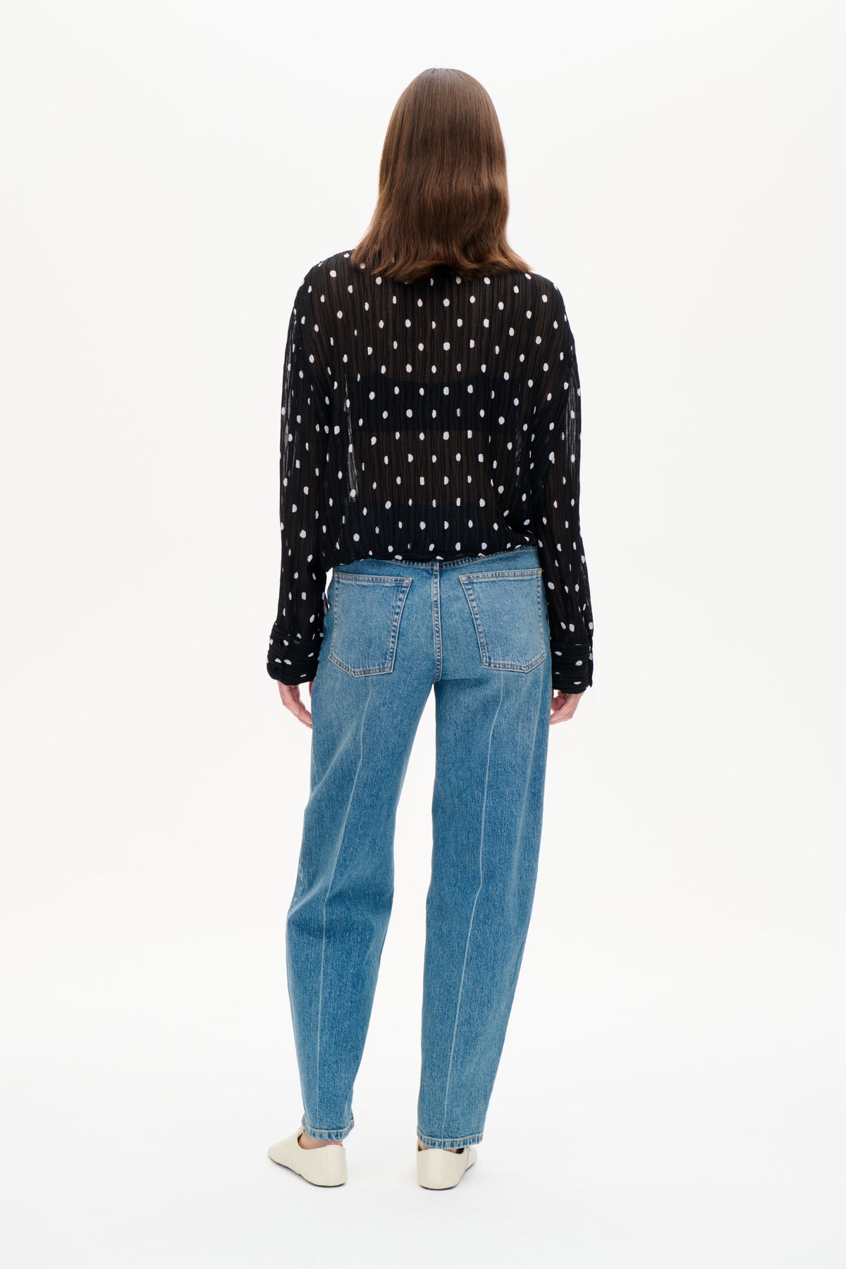 Set bagfra: en sort, let gennemsigtig bluse med lange ærmer og hvide prikker, stylet med blå jeans.
