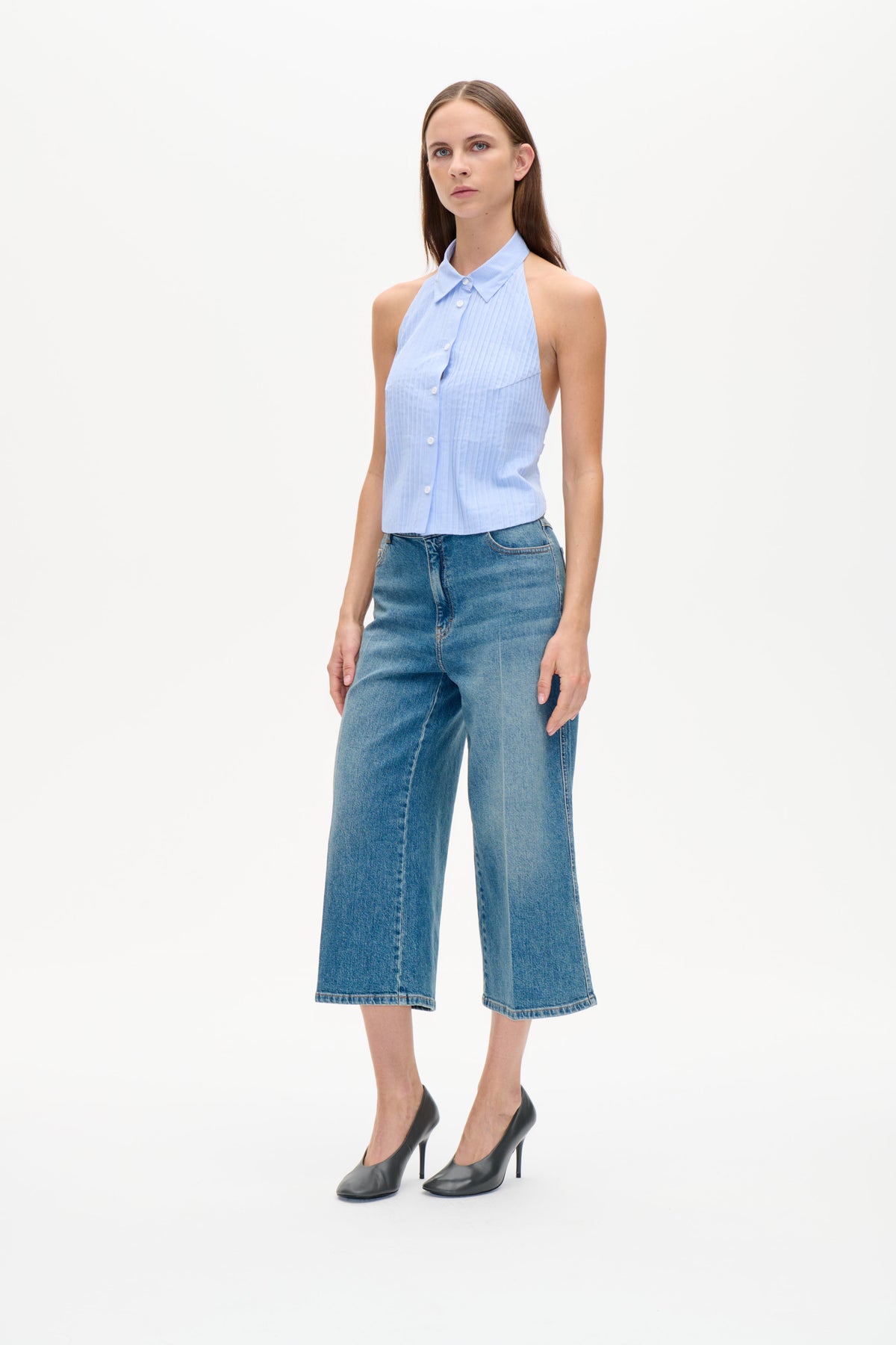 Model i lyseblå smalstribet ærmeløs top med knapper foran, spids krave og vide blå jeans.