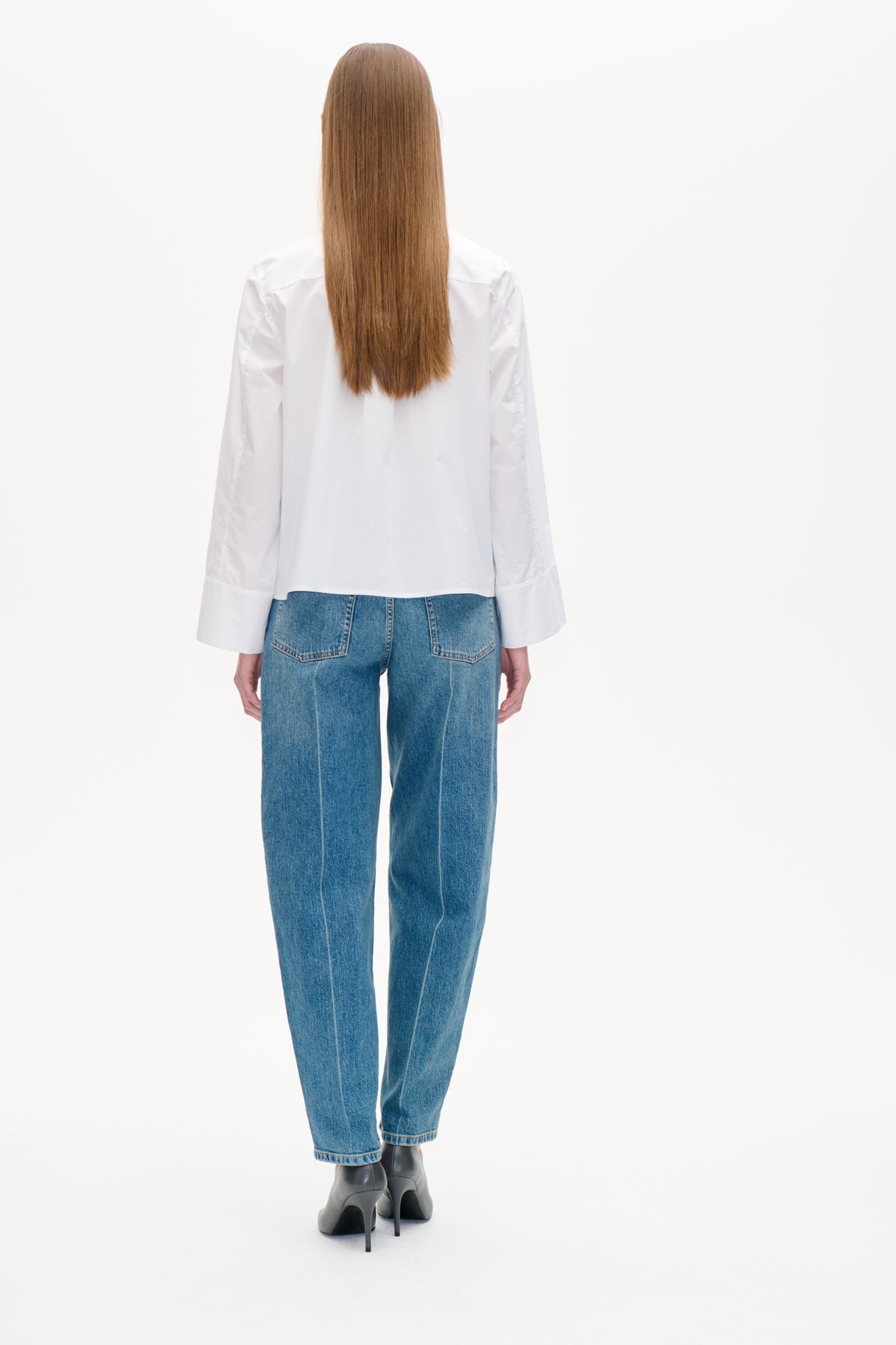 Set bagfra af en model iført en hvid langærmet bluse med brede manchetter og blå jeans med påsyede baglommer.