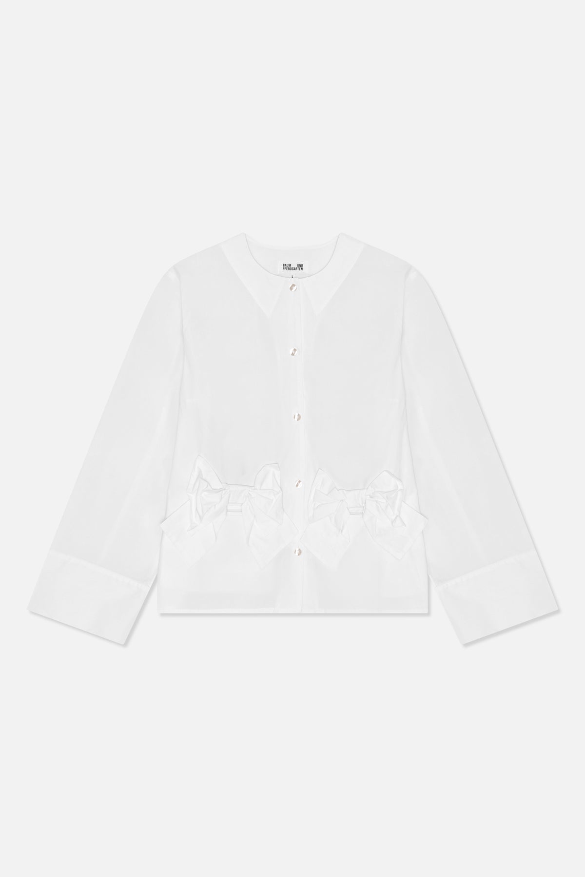 Set forfra: en hvid bluse med lange ærmer, rund hals, blanke knapper, brede manchetter og oversized sløjfedetaljer i taljen.