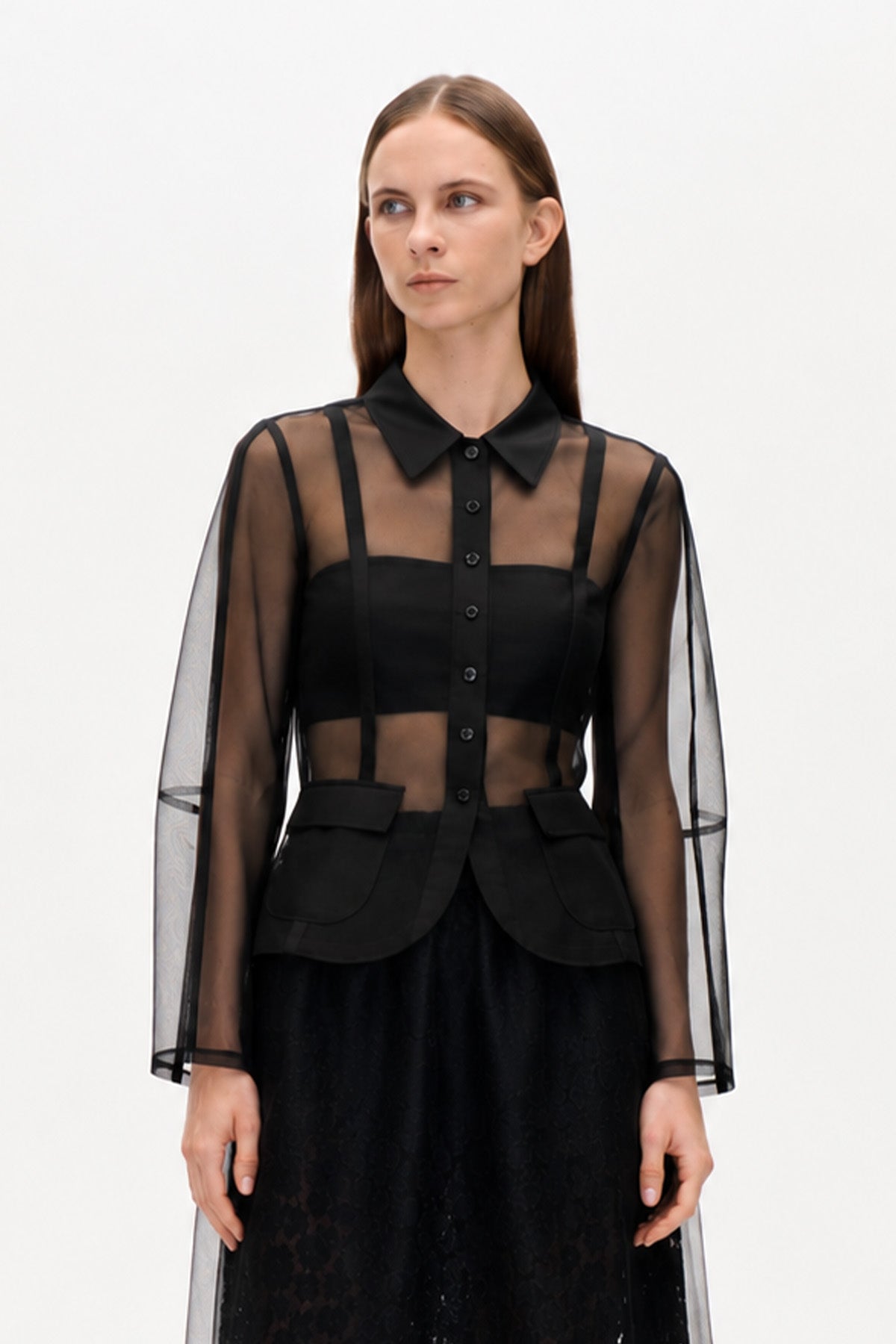 Sort transparent langærmet bluse med knapper foran, spids krave, ugennemsigtig kant og klaplommer, vist forfra.