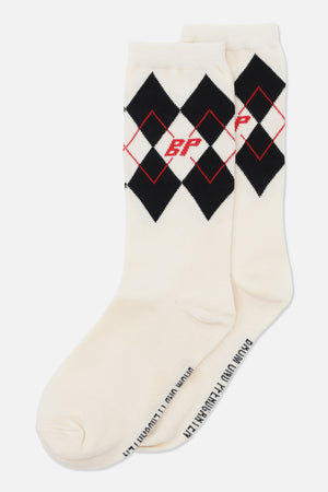 Par cremefarvede mellemlange sokker med sorte argyle-diamanter, tynde røde diamantomridser og et rødt monogram ved manchetterne.
