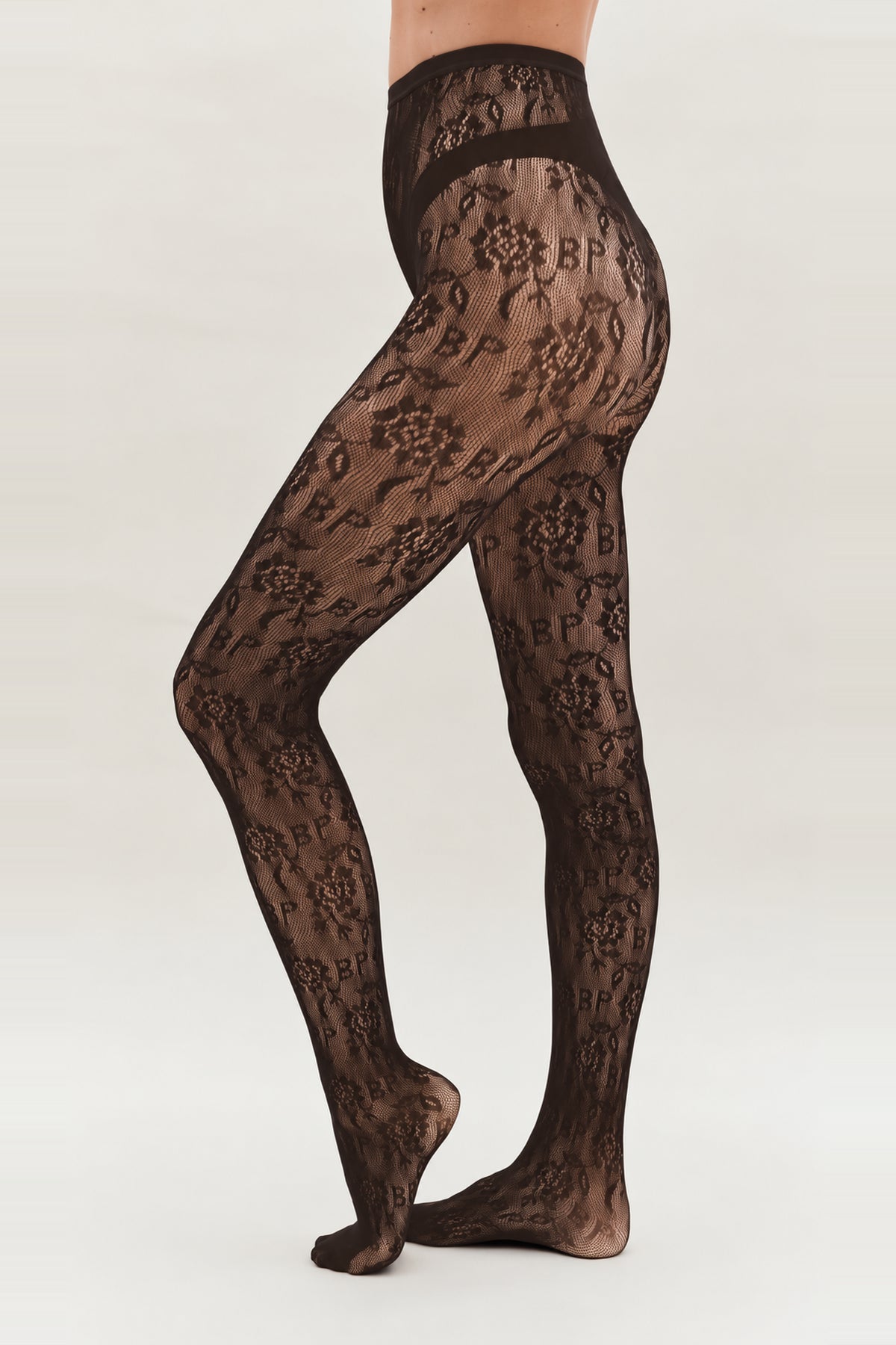Sheer black tights with floral motifs and scattered lettering, modeled from waist to feet in a side view.
