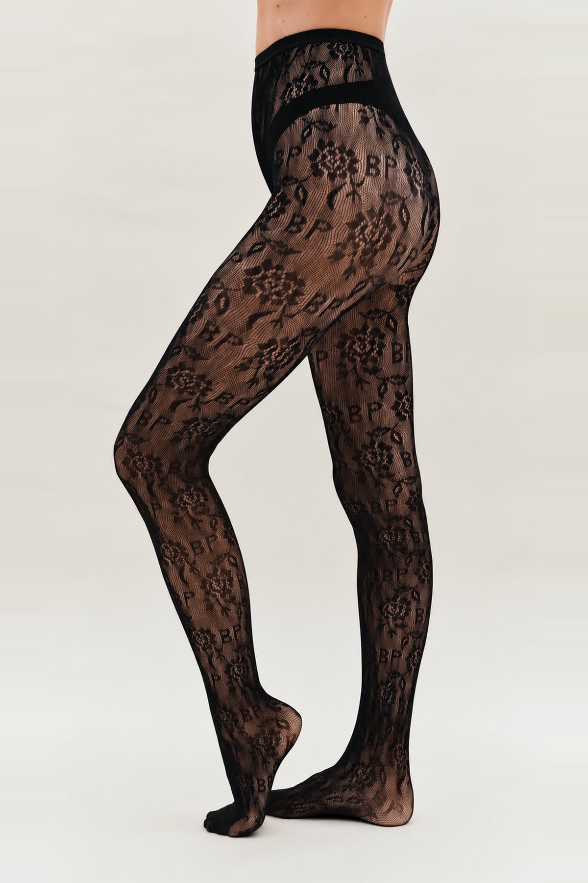 Sheer black floral-pattern tights with a wide waistband and curved opaque hip bands, modeled from waist to feet.